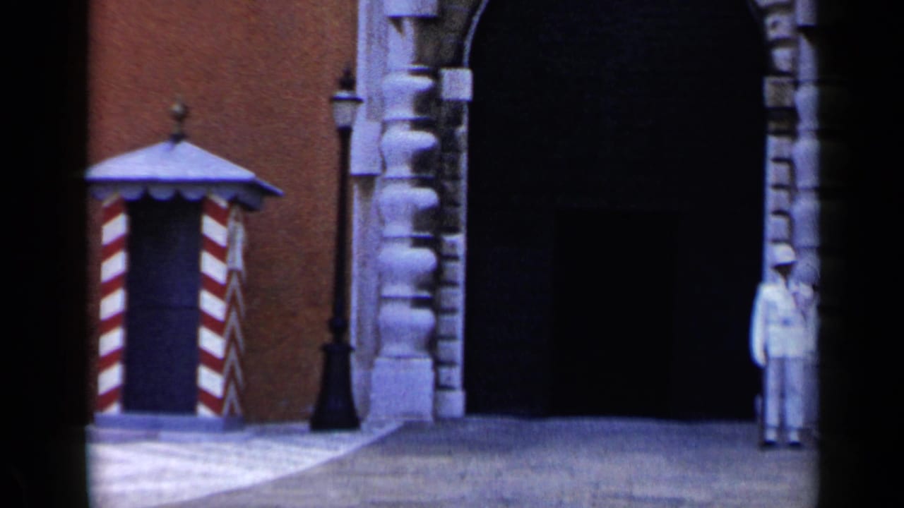 White-uniformed guard standing beside an arched building entrance and striped sentry box.