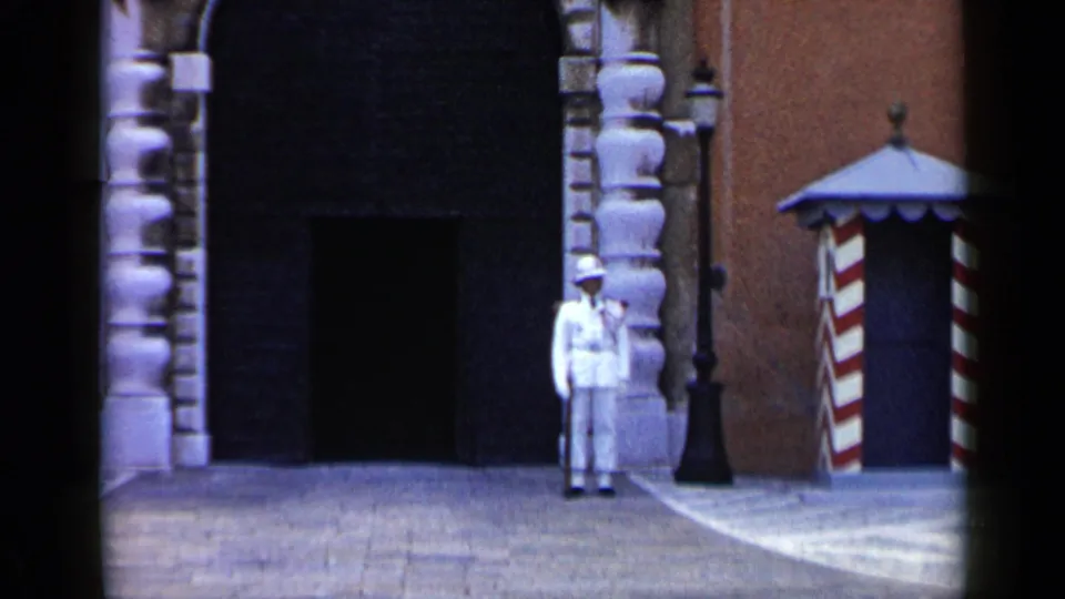 1960 Venice frame showing the guard nearer the center edge, with carved stonework, a dark doorway, and a striped sentry box visible.