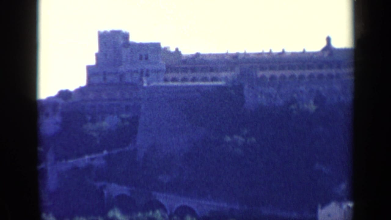Distant stone fortress on a hillside with bright sky and dark film borders.