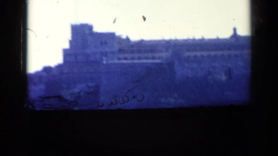 Blurred final 8mm frame of the hilltop fortification, with heavy blue cast, frame border, and visible film wear.