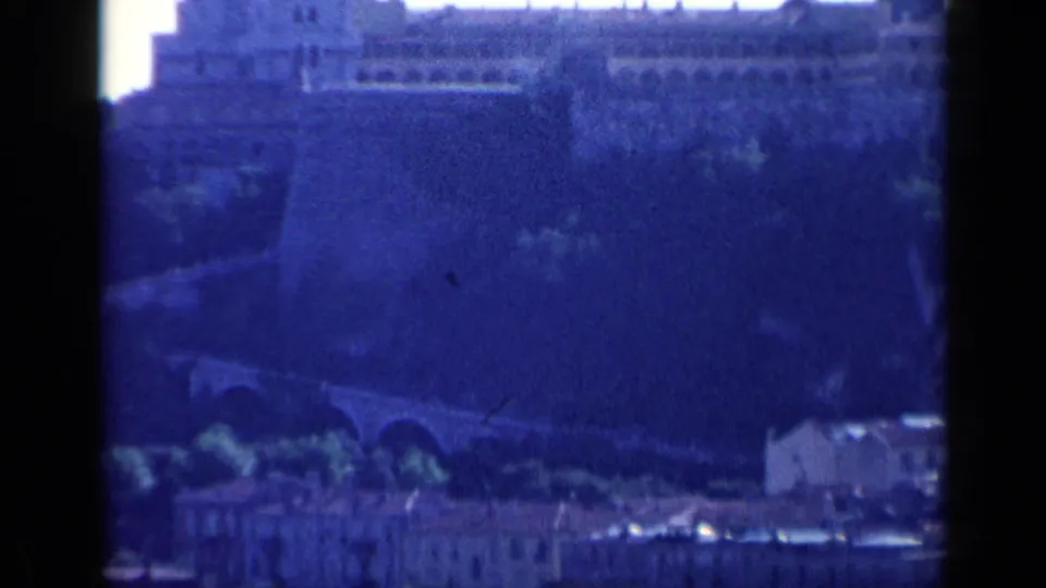 1960 Venice home-movie frame showing a distant hilltop fortification with arched approach, lower buildings, and dark 8mm frame edges.