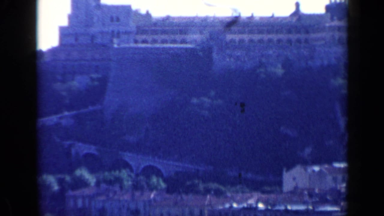 Distant blue-tinted view of a stone bridge, hillside, and pale buildings.