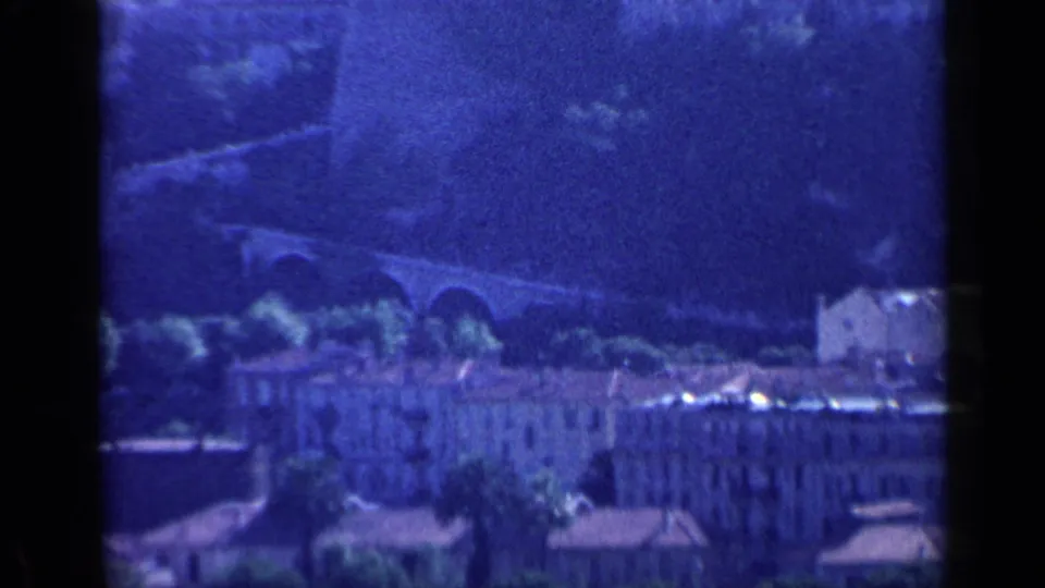 1960 8mm Venice travel frame with an arched bridge, hillside, pale buildings, and dark scan borders.