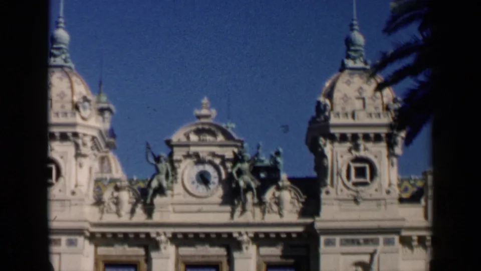 Venice, Italy 1960 8mm frame showing an ornate tan facade with a central clock, domed towers, statues, and palm fronds.