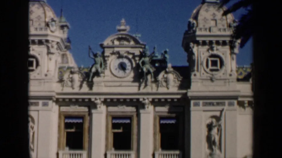 1960 Venice 8mm close view of an elaborate tan building facade with a central clock, statues, domed side towers, and tall windows.