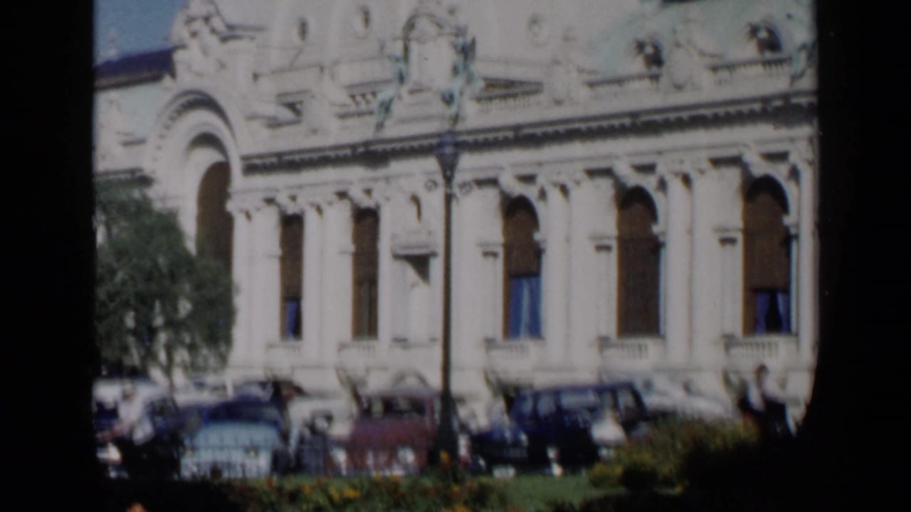 Ornate pale building facade with parked cars and trees in front.