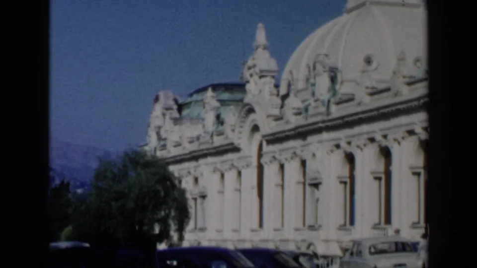 1960 Venice frame showing the ornate domed building partly framed by trees and parked mid-century cars beneath a clear sky.