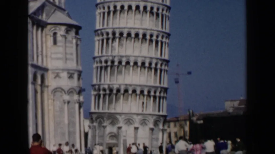 1960s 8mm travel frame showing the Leaning Tower of Pisa with small groups of tourists at its base.