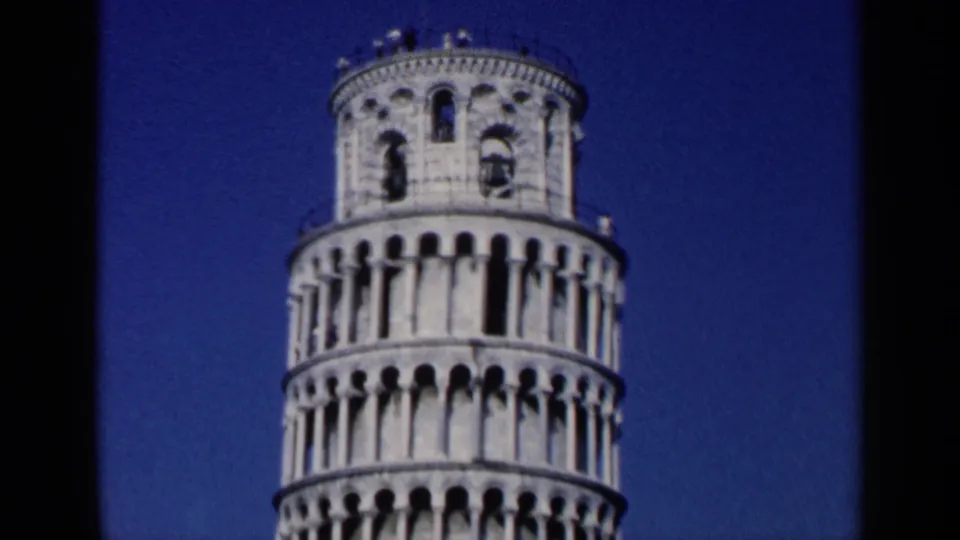 1960s 8mm close view of the upper arcades and bell level of the Leaning Tower of Pisa against deep blue sky.