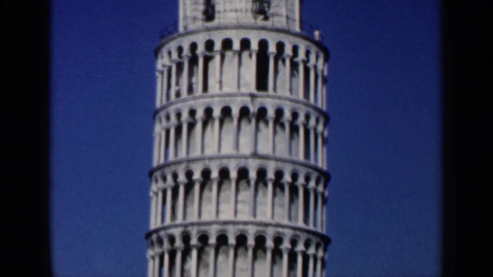 1960 Italy home-movie frame with the Leaning Tower of Pisa cropped close, emphasizing its stacked arches and tilt.