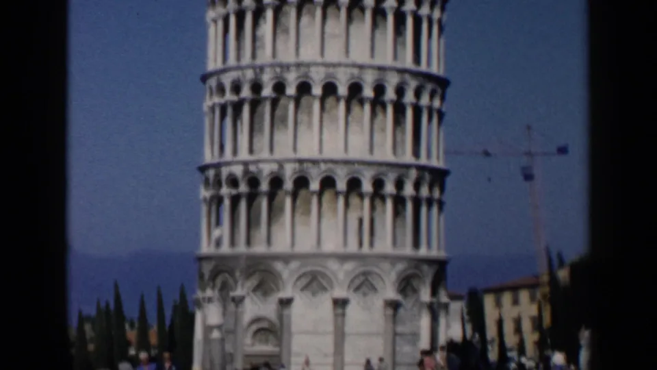 1960 Italy travel frame showing the Leaning Tower of Pisa from below, with small visitors at the base and a crane in the background.