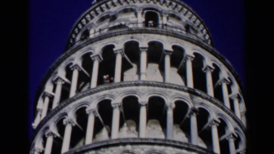 1960 8mm close-up looking upward at the Leaning Tower of Pisa, with repeated arches and columns under a deep blue sky.