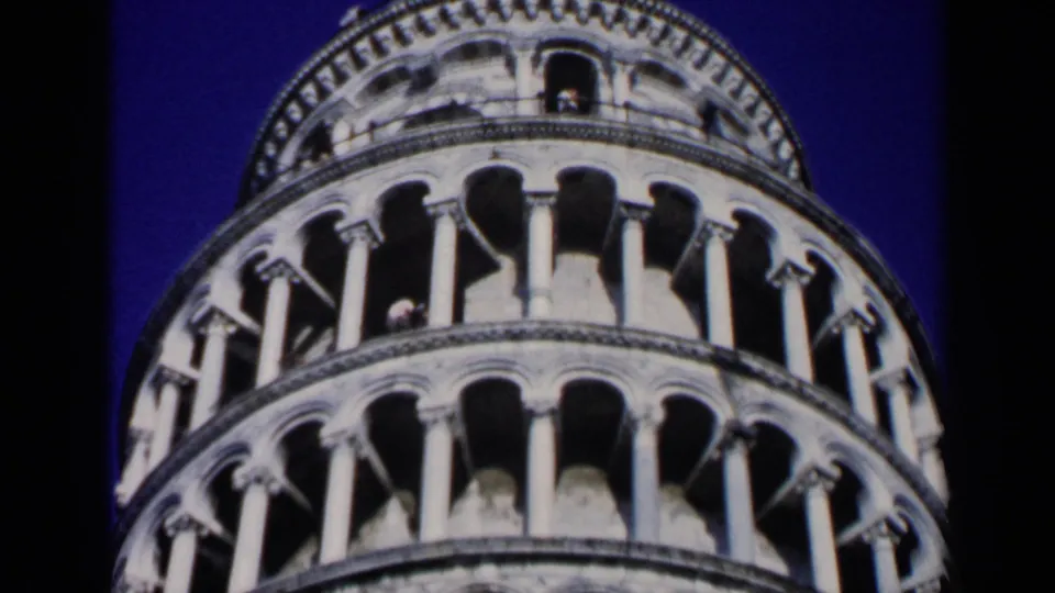 1960 8mm close view of the Leaning Tower of Pisa showing stacked arches, pale stone columns, and strong blue sky.