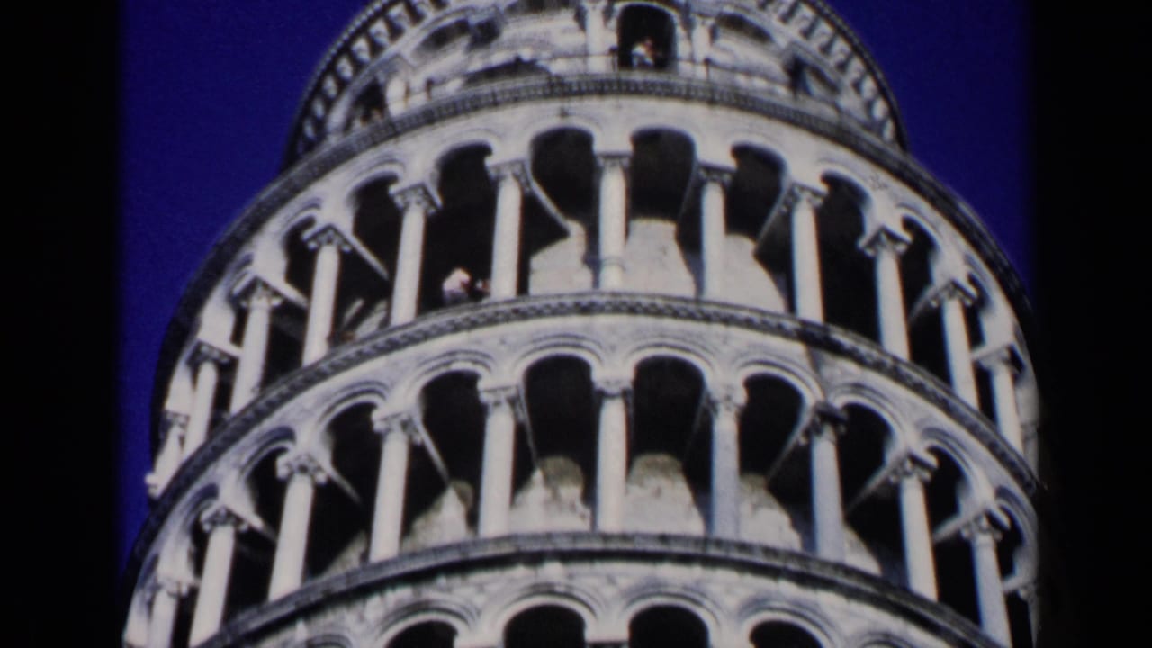 Close view of the Leaning Tower of Pisa arcades against a dark blue sky.