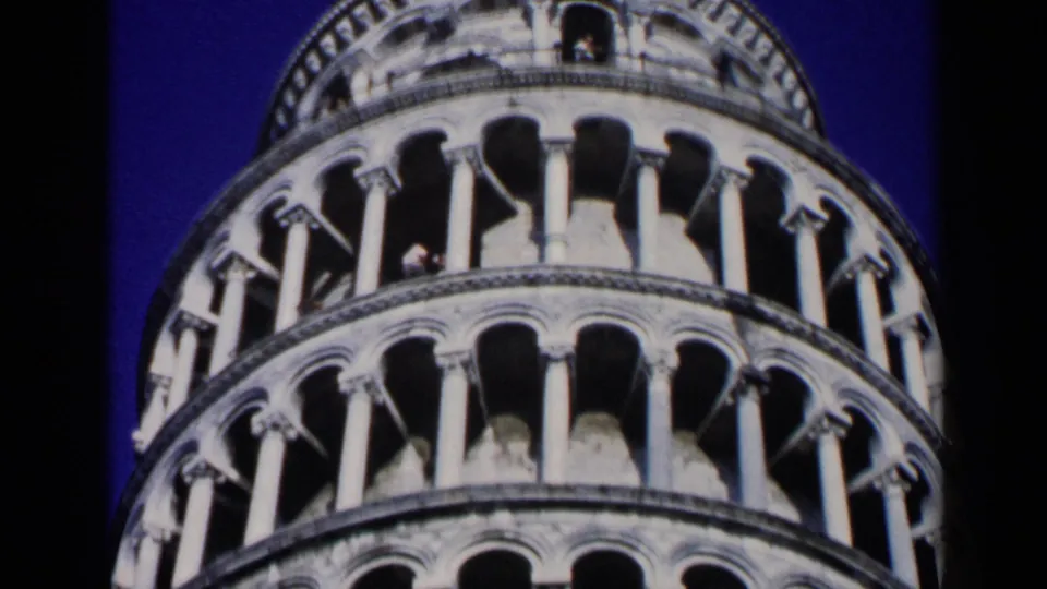 1960 8mm travel frame showing the upper arcades and columns of the Leaning Tower of Pisa, with a few distant visitors visible.