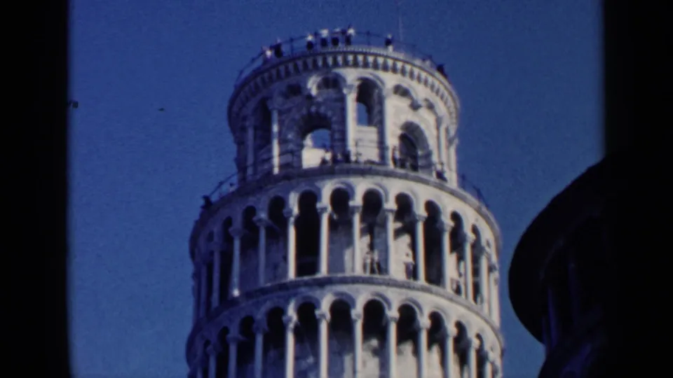 1960 8mm travel frame showing the Leaning Tower of Pisa from below, emphasizing its tilt, repeated arches, and distant visitors.