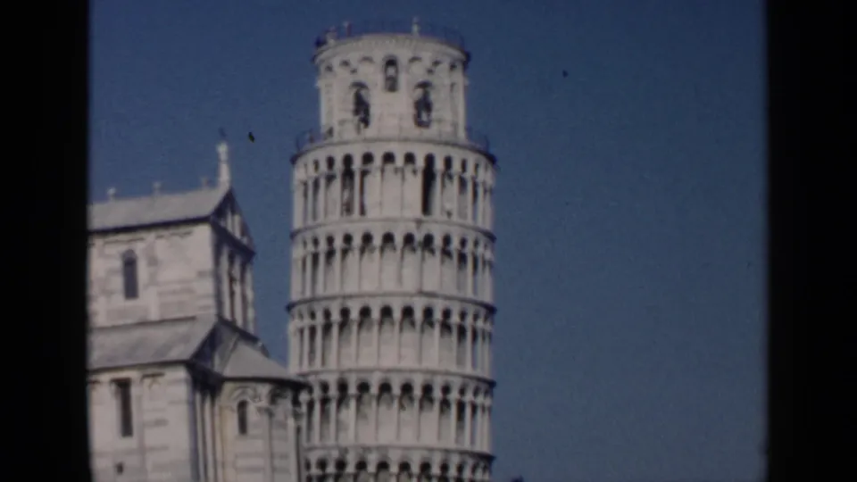 1960 8mm view of the Leaning Tower of Pisa with adjacent cathedral architecture and dark film borders.