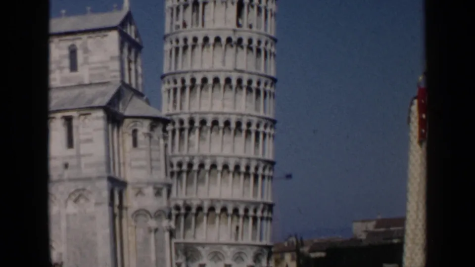 1960 8mm frame showing the Leaning Tower of Pisa next to cathedral architecture, with a narrow view of the square edge.