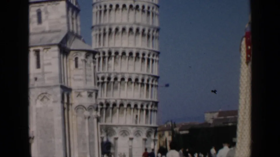 1960 8mm view of the Leaning Tower of Pisa and cathedral facade with small visitors visible near the lower edge.