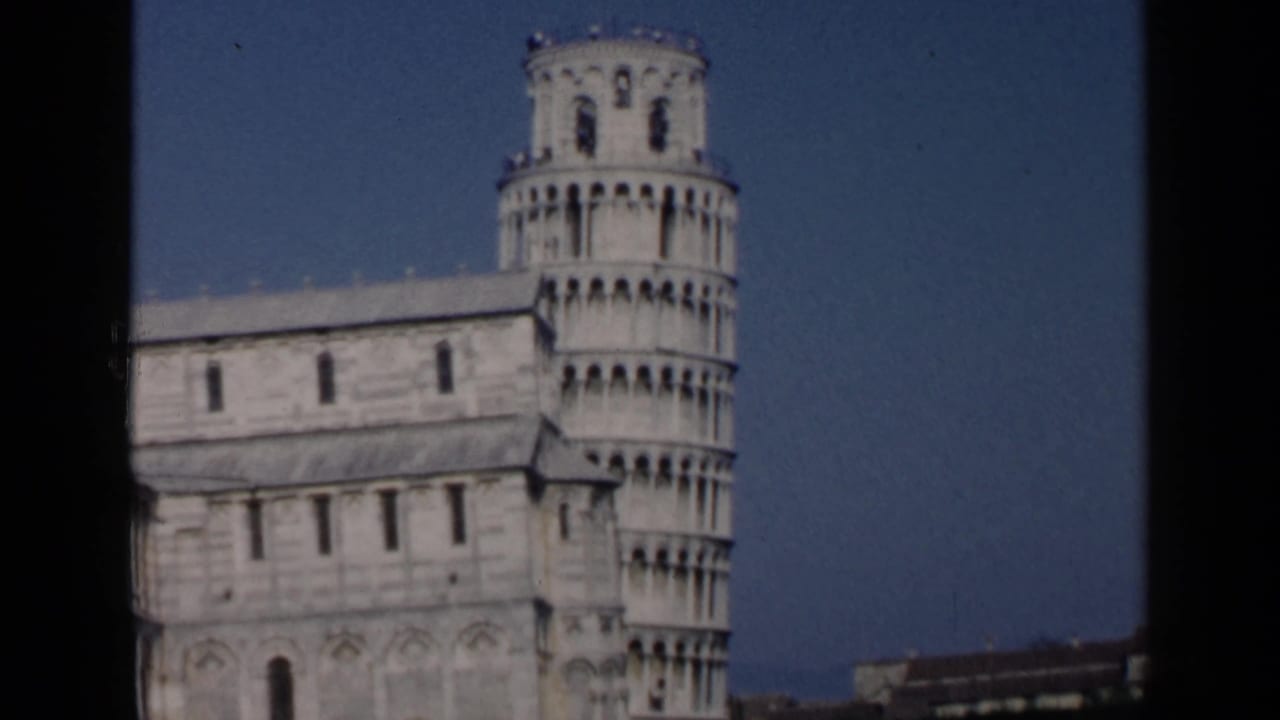 Leaning Tower of Pisa and cathedral wall seen through dark frame borders against blue sky.