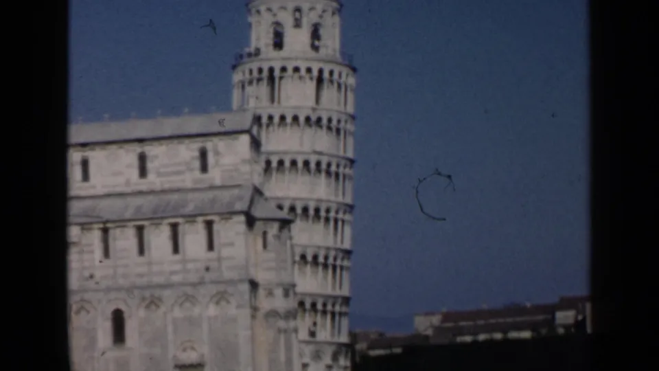 1960 home-movie frame showing the Leaning Tower of Pisa and neighboring cathedral structure, with the view partially bordered in black.