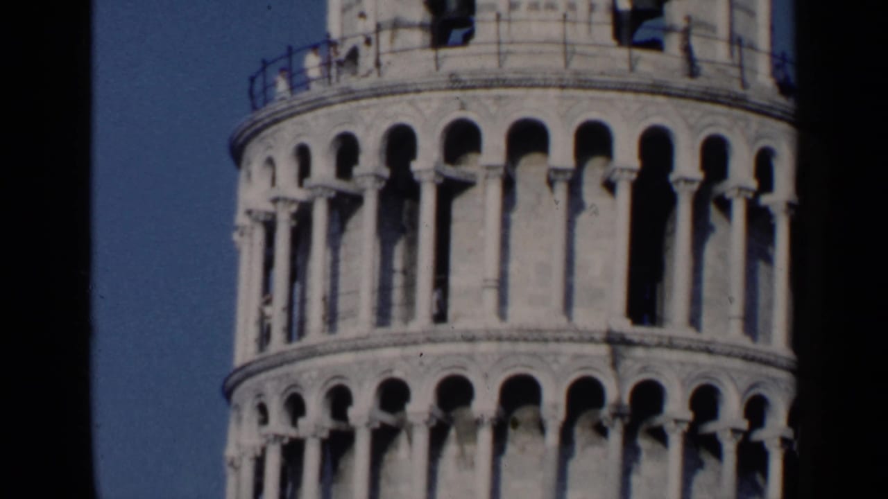 Upper tiers of the Leaning Tower of Pisa against blue sky with dark film borders.