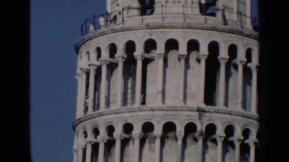 1960 8mm travel frame showing the upper arched tiers of the Leaning Tower of Pisa against a blue sky.