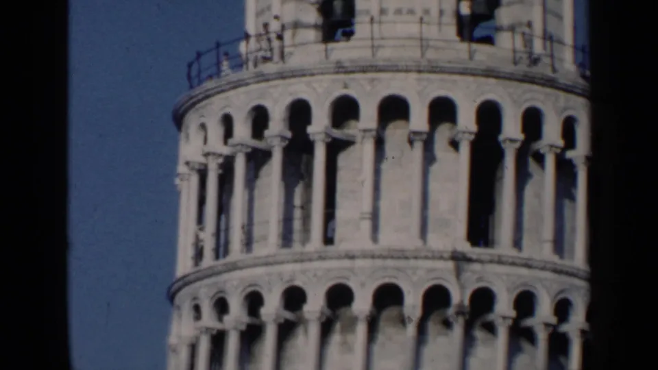 Tight 1960 home-movie view of the Leaning Tower of Pisa's upper colonnades and railing against blue sky.