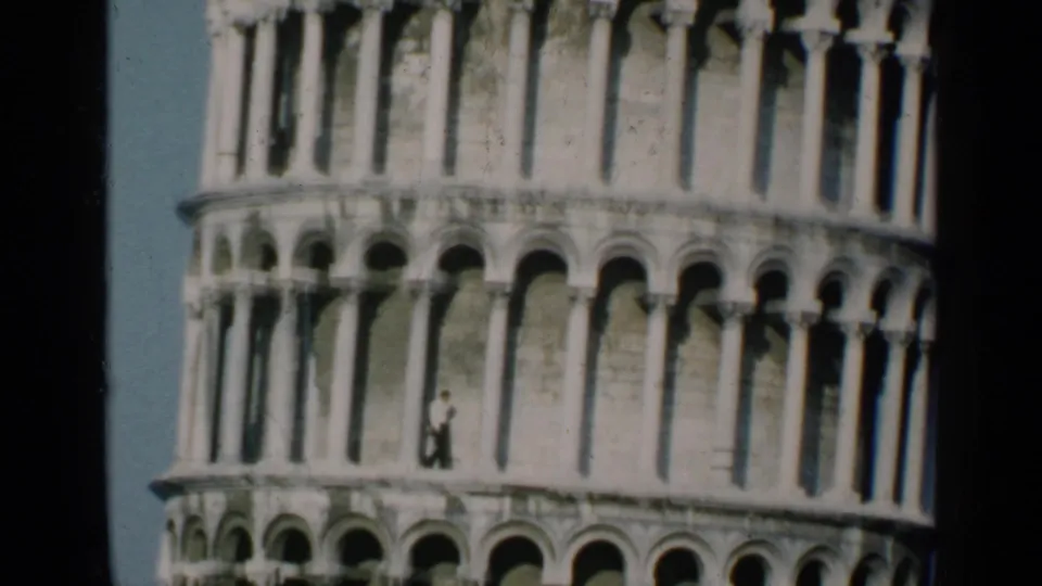 1960 8mm frame showing lower arched tiers of the Leaning Tower of Pisa with a distant visitor for scale.