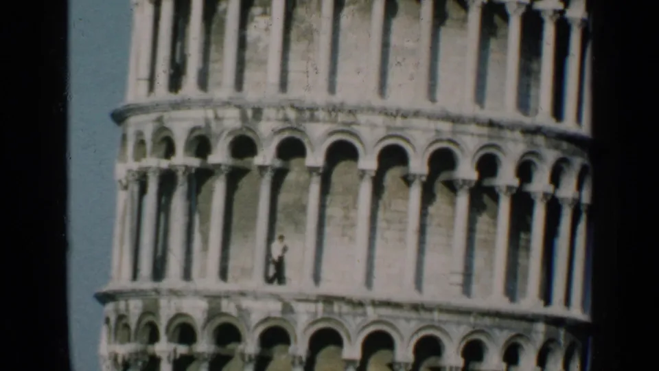 Vintage 8mm view of the Leaning Tower of Pisa midsection, with repeated arches and a distant visitor visible.