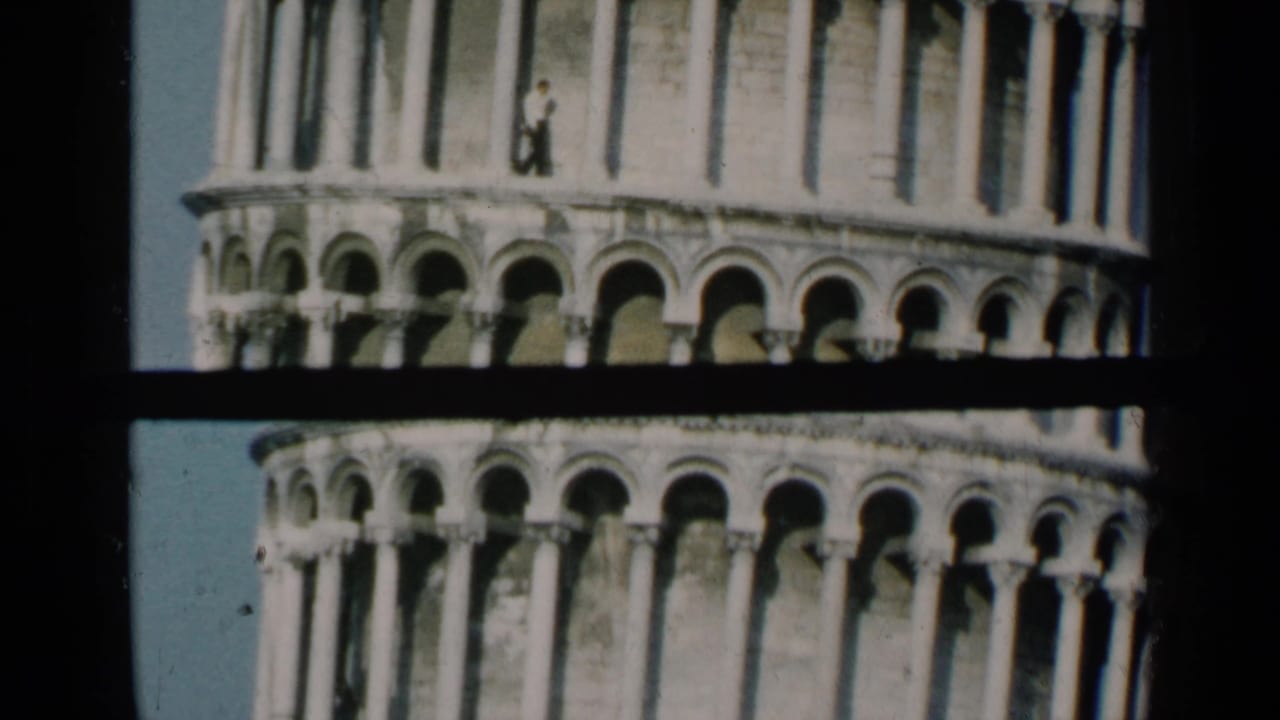 Low-angle view of the Leaning Tower of Pisa with arched levels and a small person near the upper arcade.