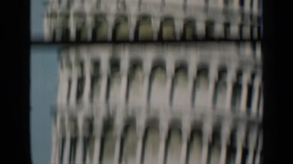 Blurred 1960s 8mm frame of the Leaning Tower of Pisa, emphasizing repeated arches and columns with heavy softness and film border at the side.