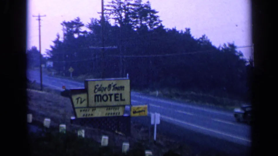 1963 California 8mm frame showing an Edge O' Town Motel sign near a two-lane highway under a blue-toned sky.