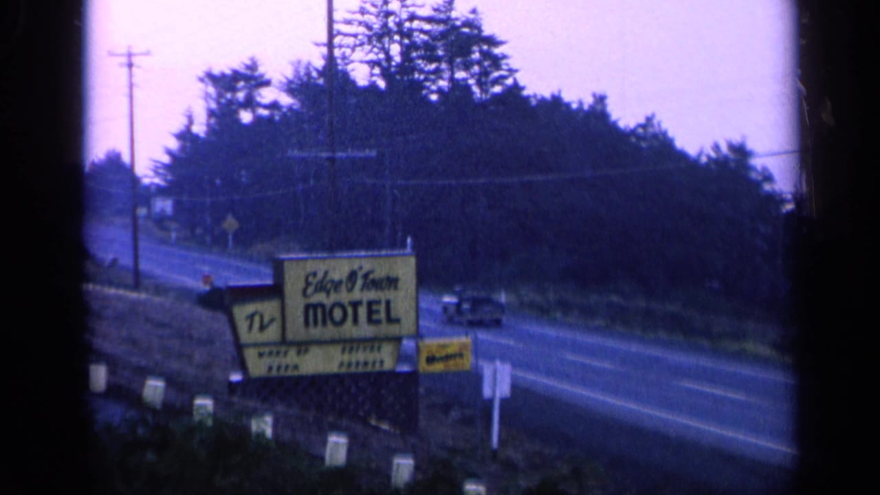 Motel sign beside the highway as a dark car passes on the road.