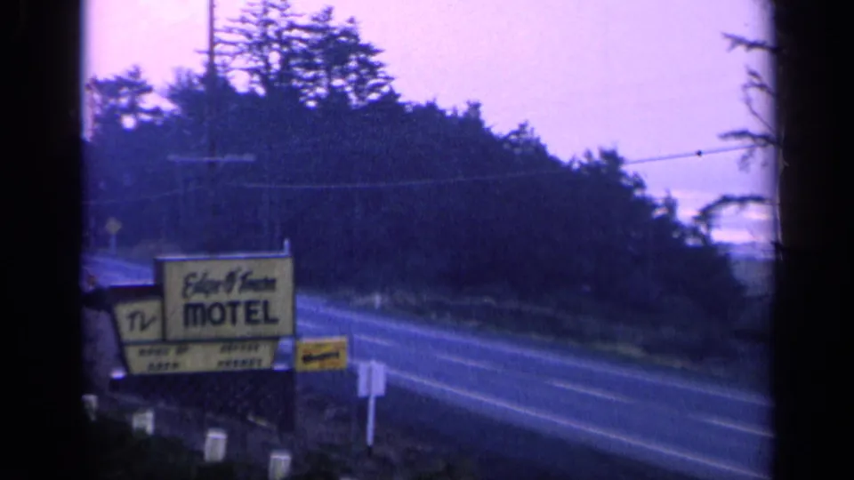 Blue-toned 8mm view of a motel sign near a California road, with trees and utility lines in the background.