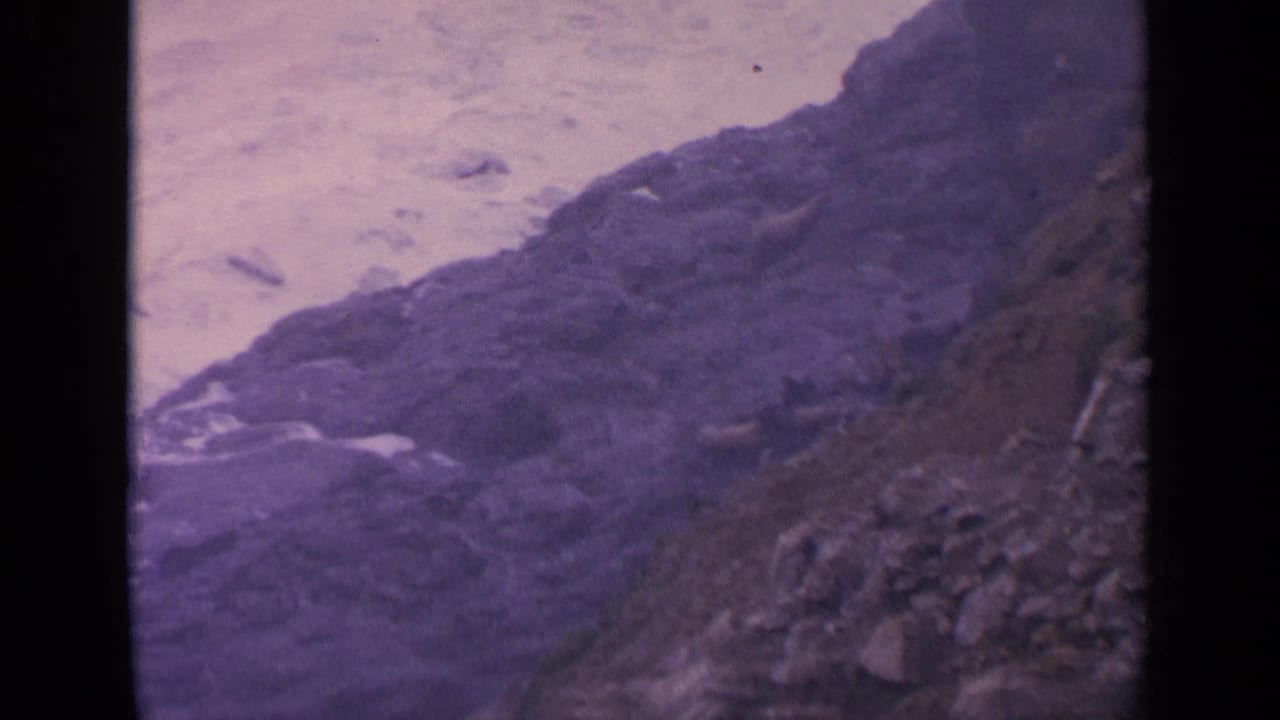 Foamy ocean water surges beside dark rocks on a rocky shoreline.