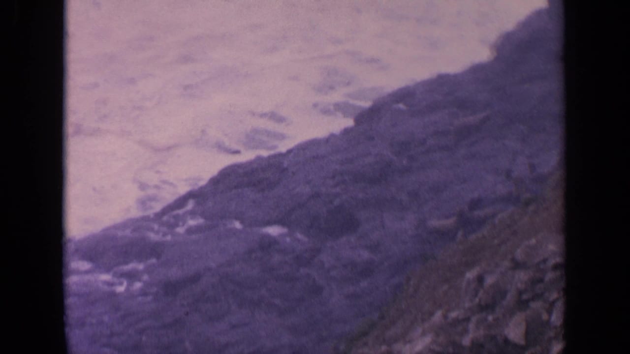 Ocean wash spreads across rocks with a dark shoreline ridge at right.