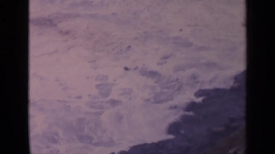 Aged 8mm view of California coastal water swirling around dark rock at the edge of the frame.