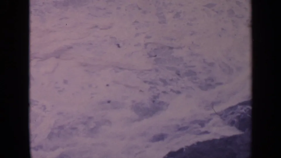 1963 California coastal frame with foamy water filling most of the view and rocks visible near the bottom edge.