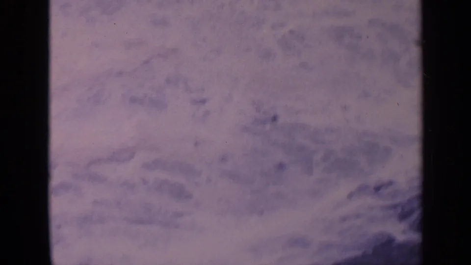 Vintage 8mm coastal frame from California showing pale surf, soft grain, and a dark rock edge.