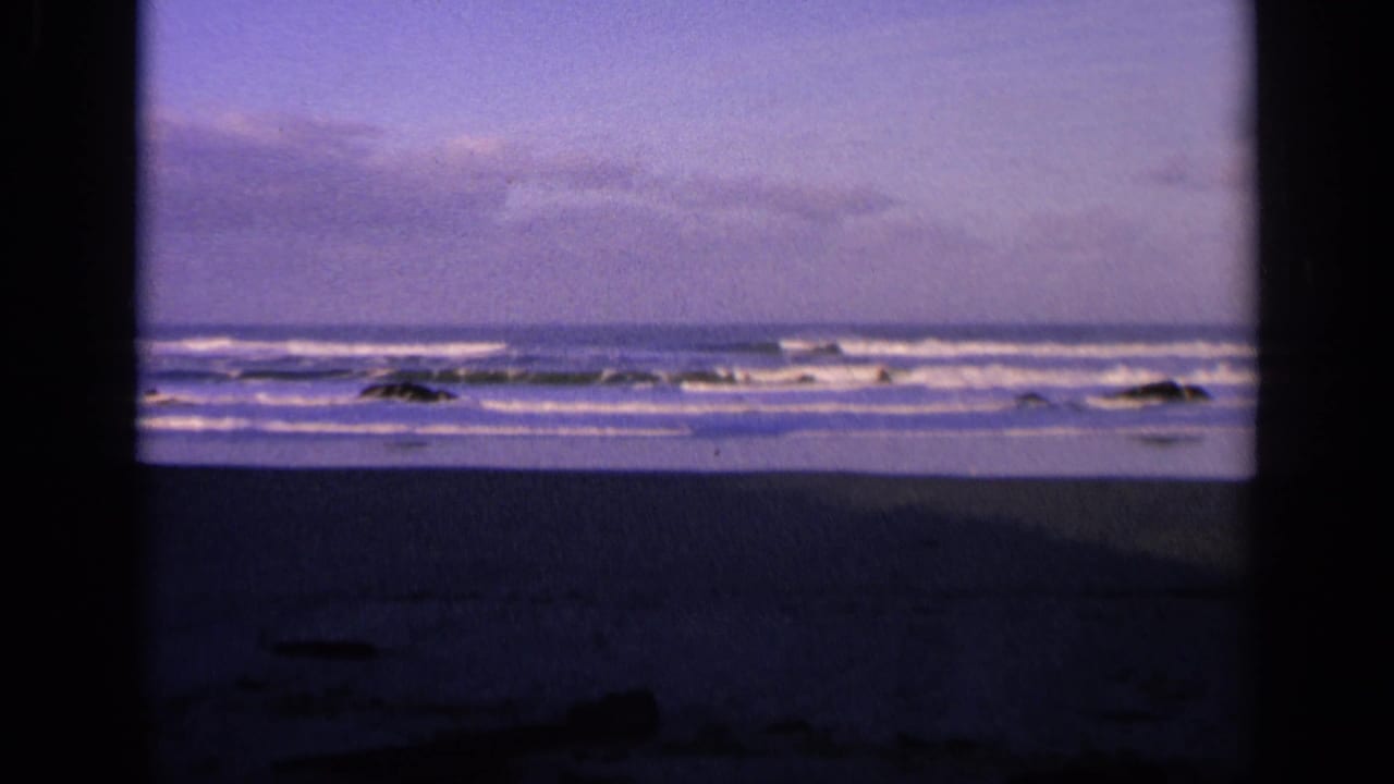 Rocky shoreline with white waves under a purple-blue cloudy sky.