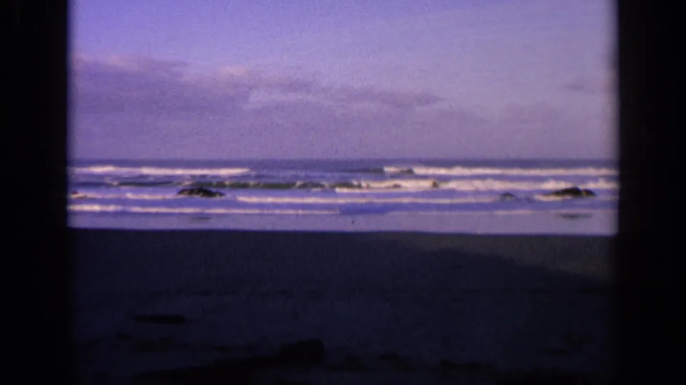 1963 California 8mm view of waves breaking across rocks and wet sand, framed by dark film edges.