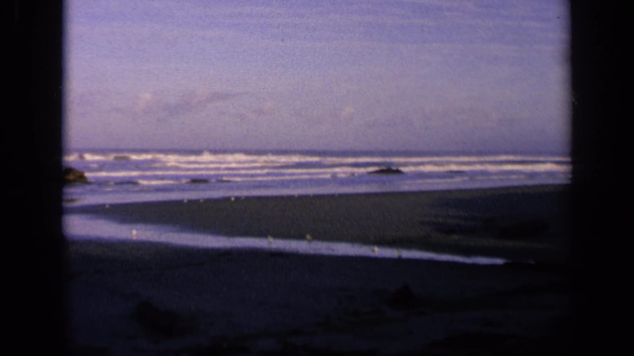 Dark-framed view of a quiet beach with waves, sand, rocks, and cloudy sky.