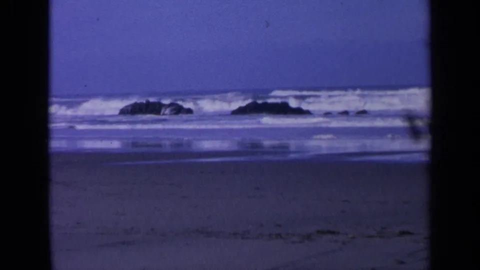 Waves break around dark shoreline rocks on a California beach, with reflective wet sand and no people visible.