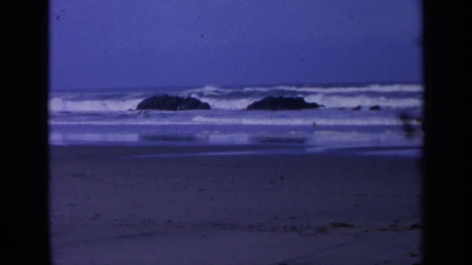 California beach footage from 1963 showing surf, distant boulders, wet shoreline, and dark 8mm frame edges.