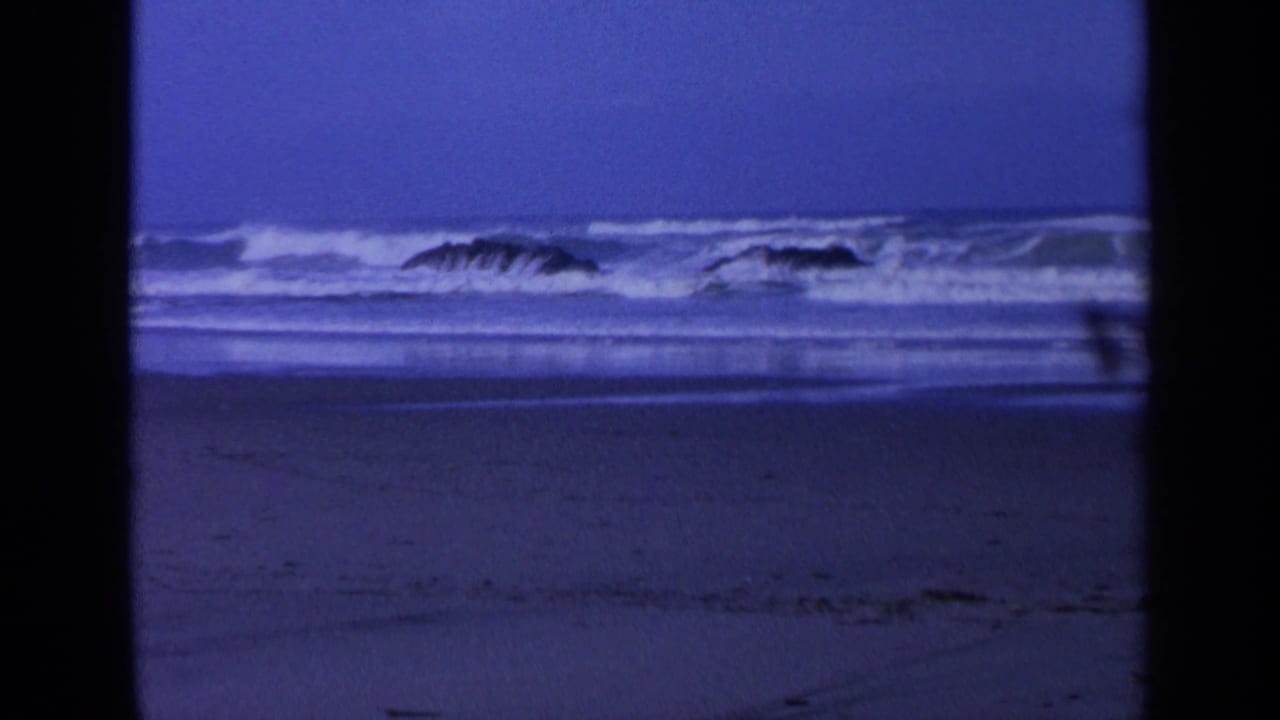Ocean waves roll toward shore around two dark rocks.