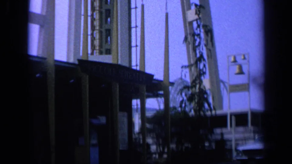1963 California 8mm frame showing a mid-century theatre exterior with columns, lamps, signage, and a parked car.