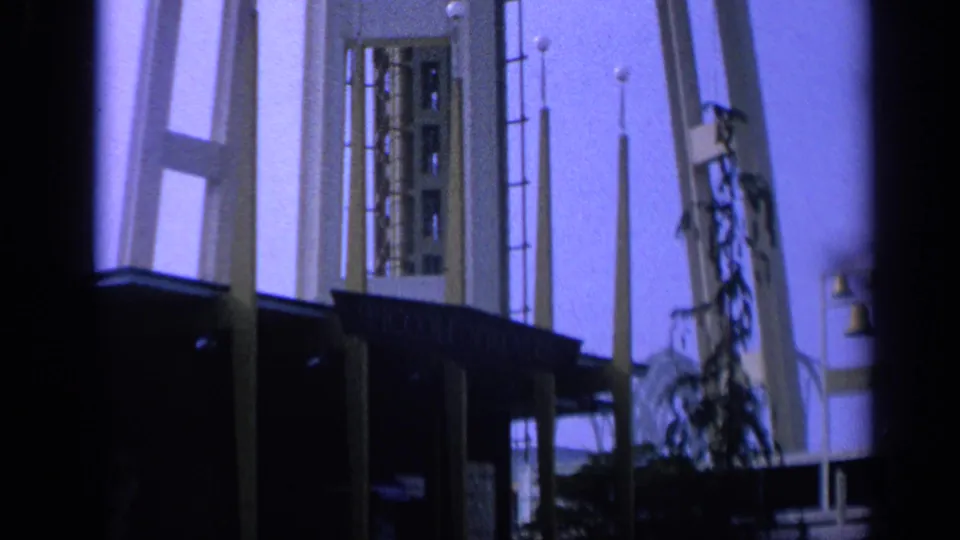 Mid-century California theatre exterior on 8mm film, with tall columns, lamps, facade details, and a parked car nearby.