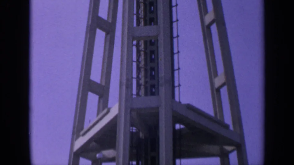 1963 California 8mm frame showing the upper part of the geometric tower with a central shaft and thin spires.