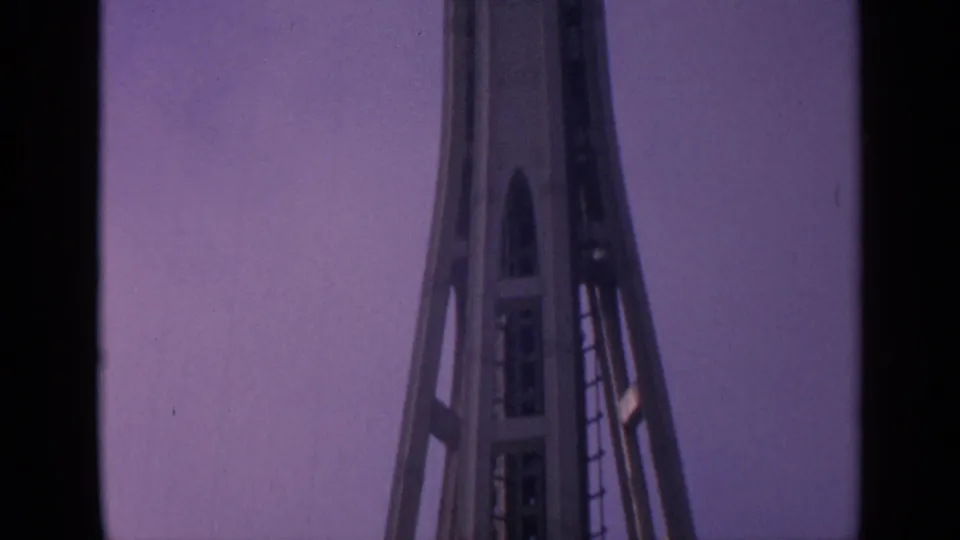 1963 8mm frame of the Space Needle upper structure rising into a purple dusky sky.